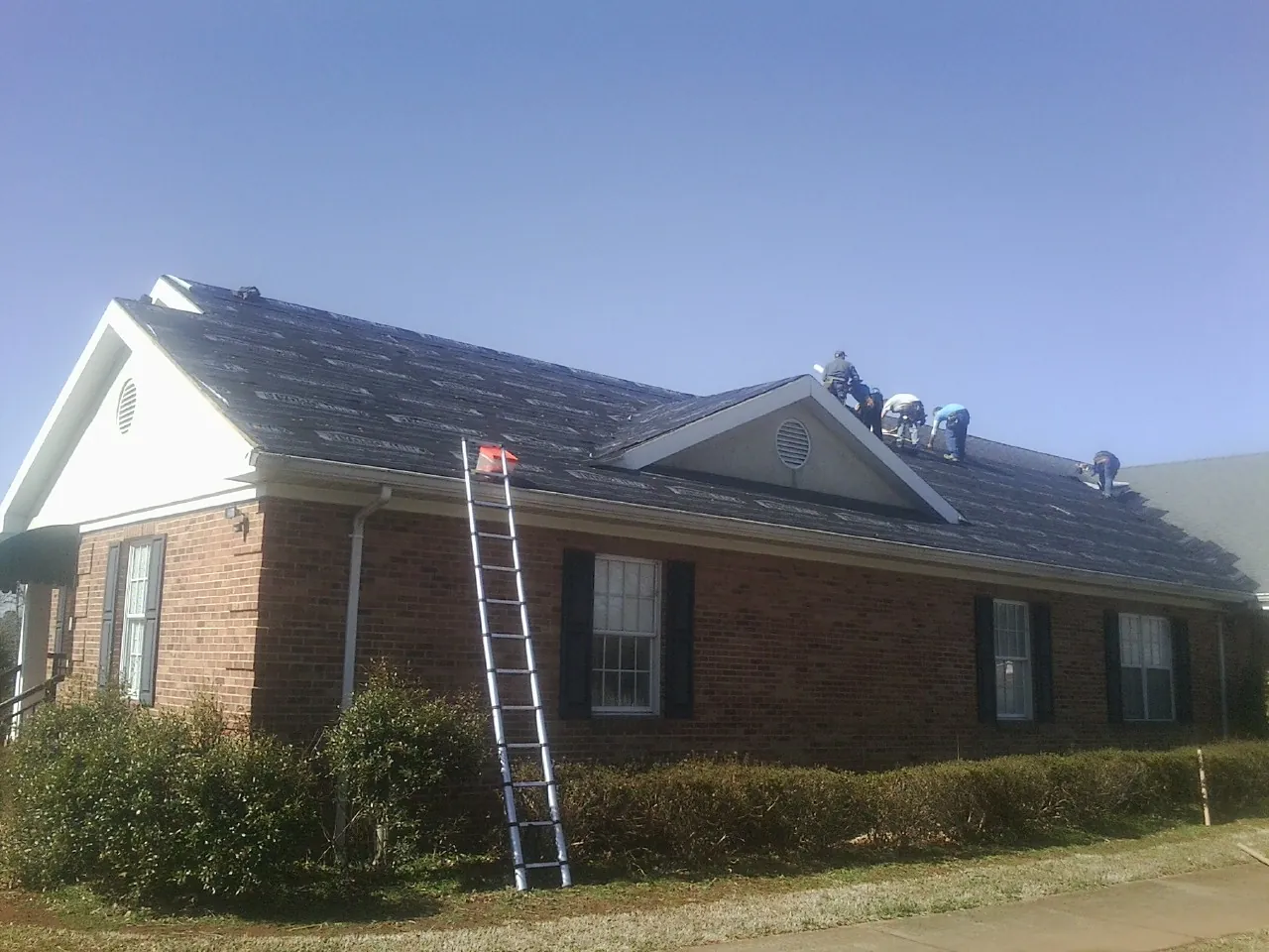 Crew tearing shingles off a brick ranch roof with a ladder set — Emergency Roof Repair work by our crew in Blythewood