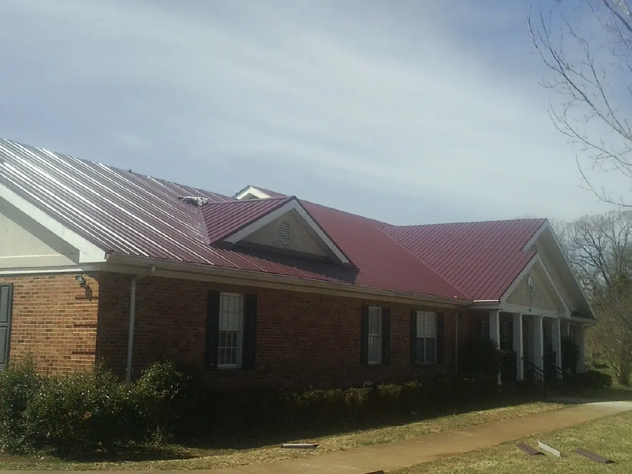 Red metal roof with gabled entries on a long brick building, from a Hail Damage Roof Repair job in Blythewood