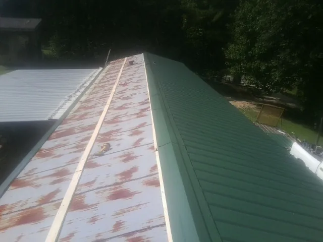 Old rusted panels beside newly installed green metal roofing — Wind Damage Roof Repair by Roofing Brothers in Blythewood