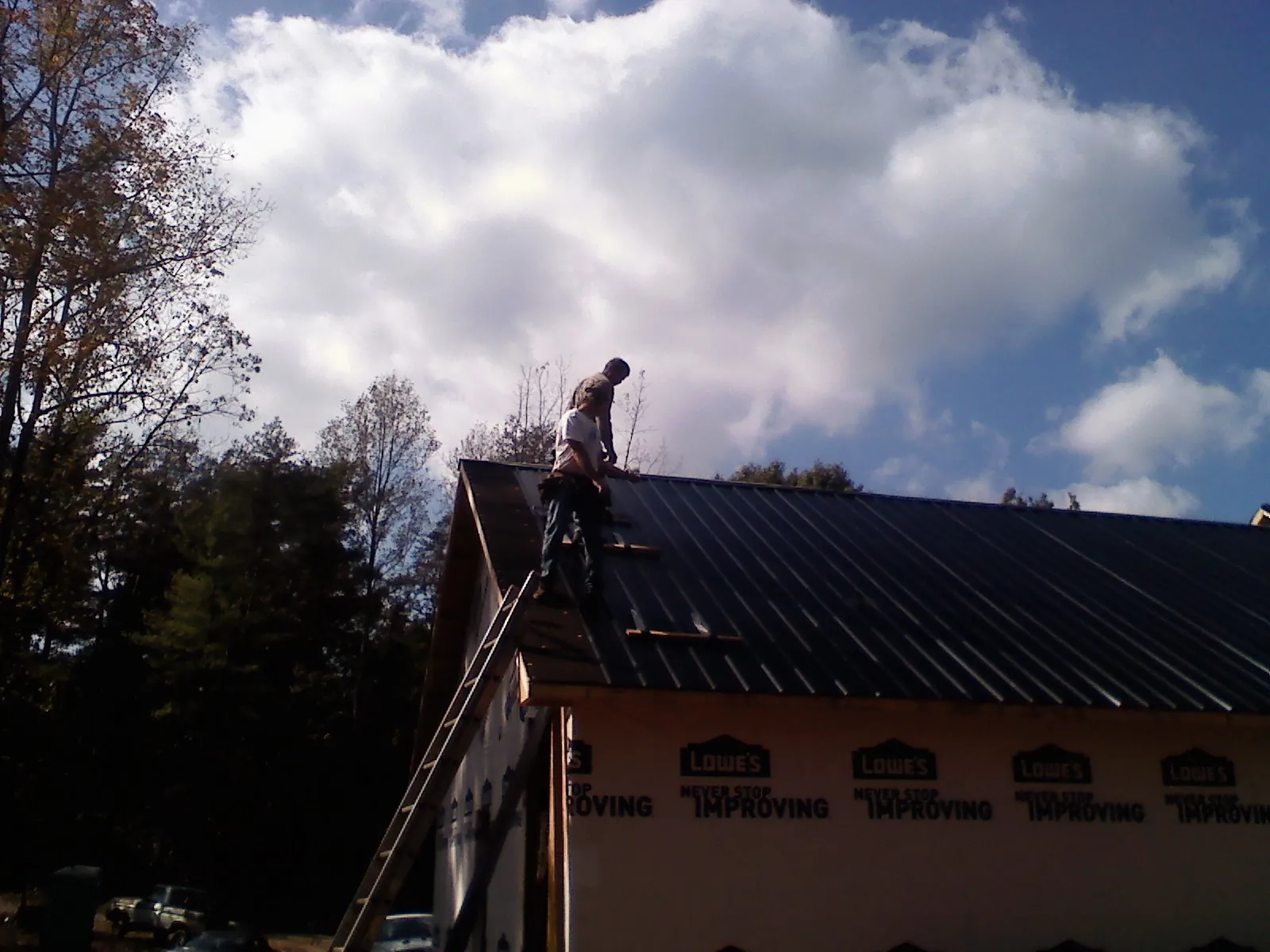 Roofer fastening dark metal panels high against a cloudy sky, from a Roof Inspection job in Blythewood