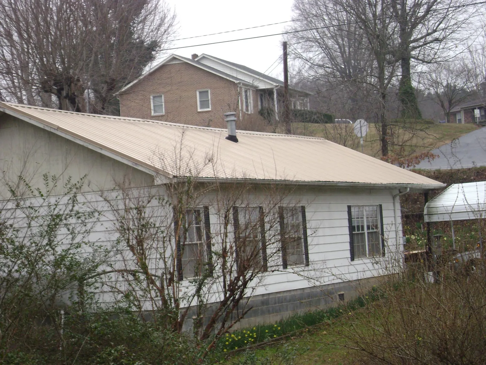 Tan metal roof on a white sided house set into a hillside — Commercial Roofing by Roofing Brothers in Blythewood